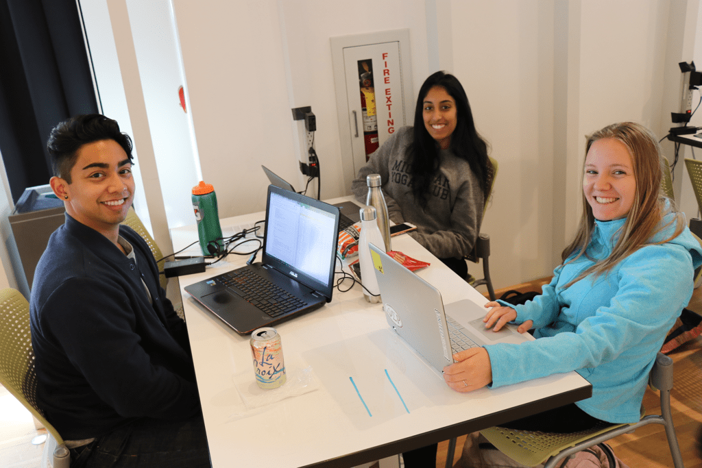 Three students at their laptops participating in the hackathon