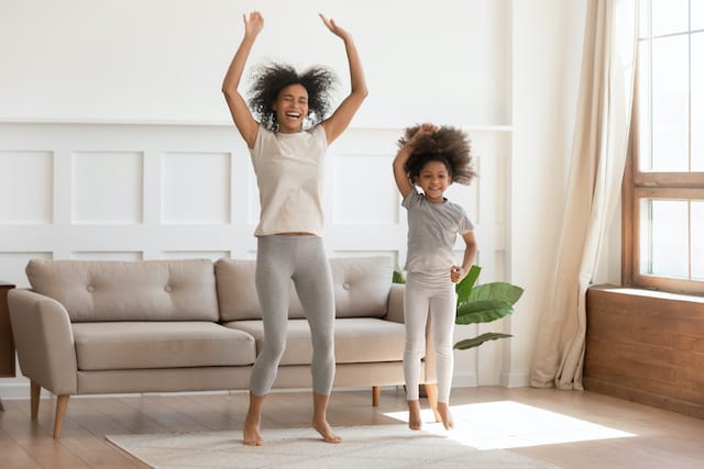 African mom with kid girl jumping dancing in living room